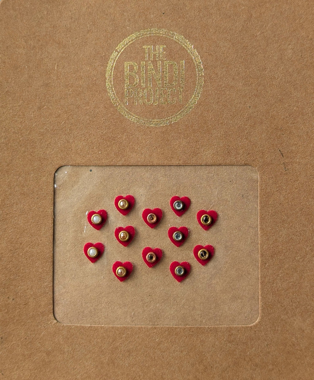 Set of 12 small maroon heart-shaped bindis with central white and black stones on brown card packaging.