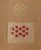 Set of 12 small maroon heart-shaped bindis with central white and black stones on brown card packaging.