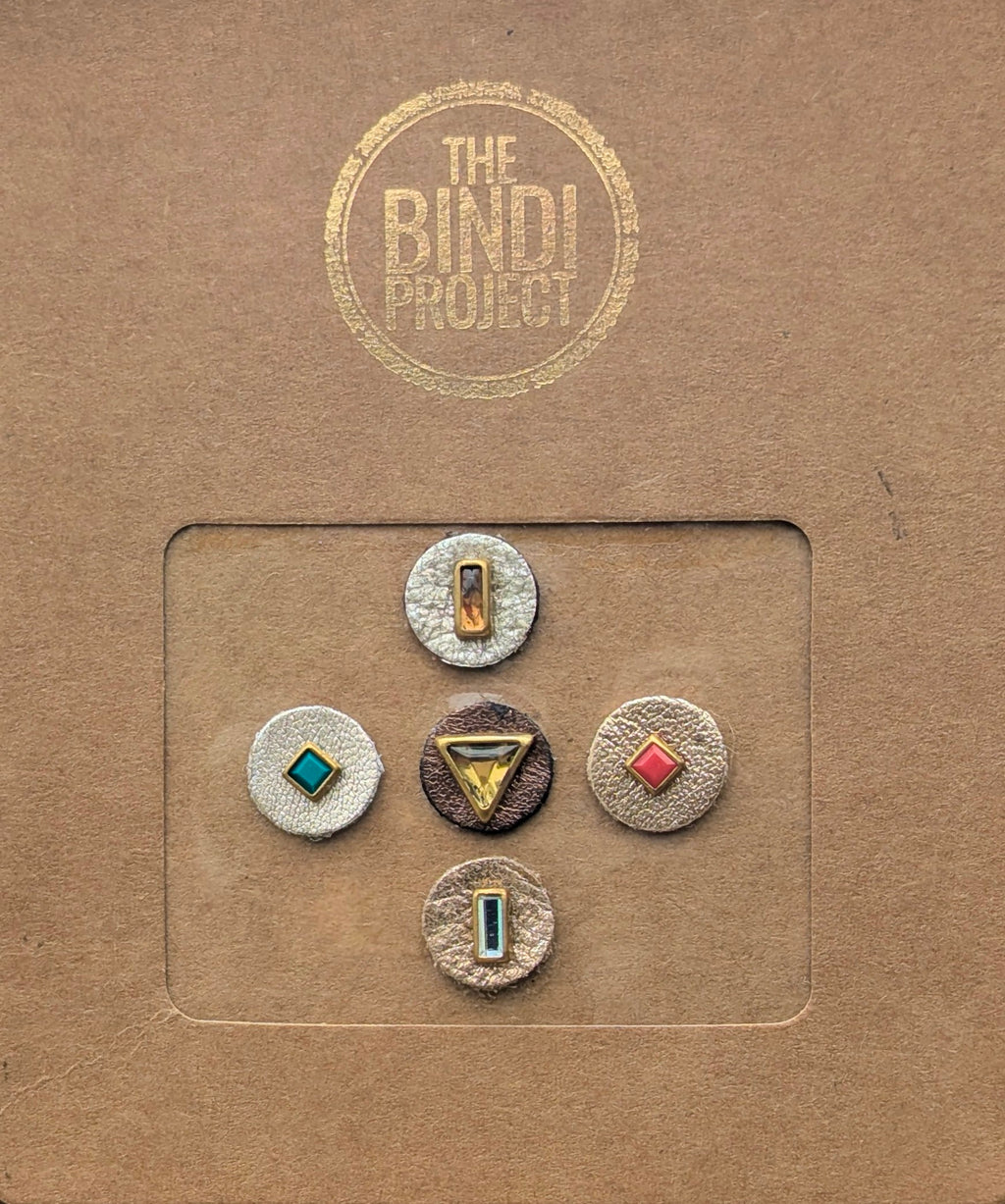 Set of five artisanal 14mm leather bindis with geometric metallic and colorful stone accents on a brown card.