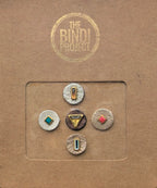 Set of five artisanal 14mm leather bindis with geometric metallic and colorful stone accents on a brown card.