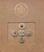 Five artisanal leather bindis in gold, turquoise, and black with geometric and teardrop designs on brown branded packaging.